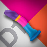 A vibrant Avant D1 Hot 'n' Cool 6" Non-Porous Silicone Dildo from Avant, featuring a deep suction cup base, is showcased against a lively geometric backdrop in shades of pink, purple, blue, orange, and gray. The dildo's design includes a gradient effect with a slight curve and a tapered tip.
